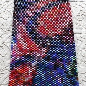 May include: A beaded bracelet with a colourful abstract design featuring shades of red, blue, and purple.