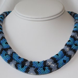 May include: A double-strand beaded necklace with a blue, black, and gray geometric pattern.