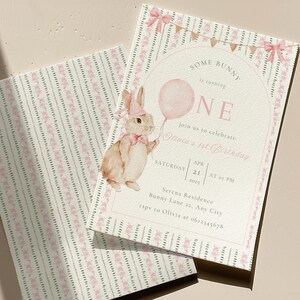 Op de afbeelding: Tweeledelige uitnodigingsset voor een eerste verjaardag. De uitnodiging toont een aquarel illustratie van een konijn met een roze ballon. De tekst luidt "Some Bunny is turning ONE" en bevat evenementdetails.