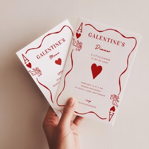 Op de afbeelding: Twee witte Galentine's diner uitnodigingen met rode accenten. De uitnodigingen bevatten de tekst "GALENTINE'S Dinner" en "A LITTLE DINNER A LOT OF LOVE". Elke kaart heeft een rood hart en cupid illustraties.