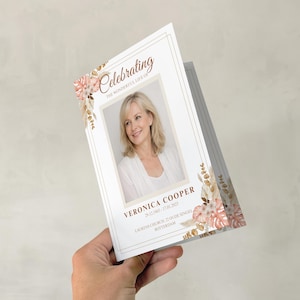 Op de afbeelding: Een witte herdenkingskaart met een foto van een vrouw, omlijst door een gouden rand en bloemmotieven. De kaart bevat de tekst "Celebrating the Wonderful Life of Veronica Cooper" en persoonlijke details.