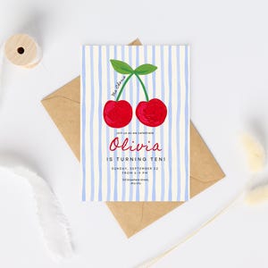 Pu&ograve; includere: Un invito di compleanno con un'illustrazione di ciliegie. La carta ha strisce blu e bianche e il testo "Olivia compie dieci anni!" L'invito &egrave; su una busta marrone.