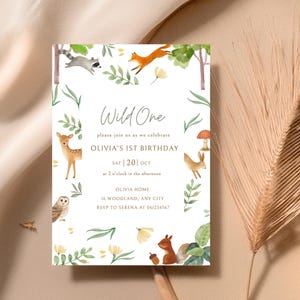 Puede incluir: Una invitación caprichosa para el primer cumpleaños de Olivia, con animales del bosque y detalles del evento. El diseño incluye el texto "Wild One", rodeado de vegetación verde y flores amarillas. La invitación está sobre un fondo neutro.