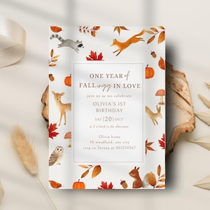 Op de afbeelding: Een uitnodigingskaart met een bos thema, met illustraties van bosdieren en herfstbladeren. De tekst luidt "ONE YEAR of FALLING IN LOVE" en kondigt een eerste verjaardag aan. De kaart is versierd met pompoenen, bladeren en paddenstoelen.