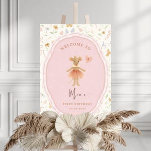 May include: A pink and cream-colored birthday sign featuring a cartoon mouse holding a balloon. The sign reads "Welcome to Mia's First Birthday 22.09.2025" in elegant script. The sign is decorated with floral and butterfly motifs.