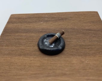 May include: A small black ashtray with a brown cigar resting on top. The ashtray is filled with white ash.