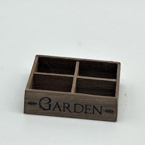 May include: A wooden box with four compartments, labeled "GARDEN" with an arrow on each side. The box is brown and has a rustic look.