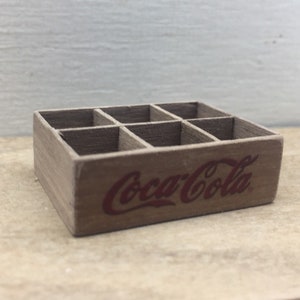 May include: A wooden crate with six compartments, painted brown with a red Coca-Cola logo.