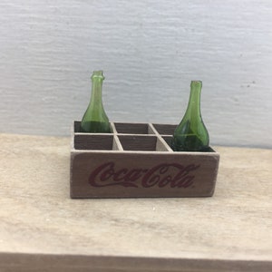 May include: A miniature wooden Coca-Cola crate with two green glass bottles inside.
