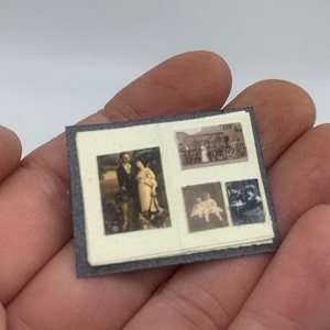 May include: A small black photo album with four black and white photos inside. The photos show a couple, a group of people, and two other individuals.