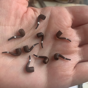 May include: A collection of miniature wooden pipes with silver accents. The pipes are arranged on a hand, with the bowl of each pipe facing upwards.
