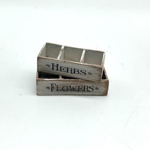 May include: Two white wooden boxes with brown trim. The top box has the word "HERBS" printed on it. The bottom box has the word "FLOWERS" printed on it.