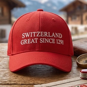 Könnte beinhalten: Eine leuchtend rote Baseballkappe mit weißem Sticktext, der SWITZERLAND GREAT SINCE 1291 lautet. Die Kappe verfügt über eine strukturierte Krone, einen gebogenen Schirm und einen Knopf an der Oberseite als klassisches Kopfbedeckungsstück.