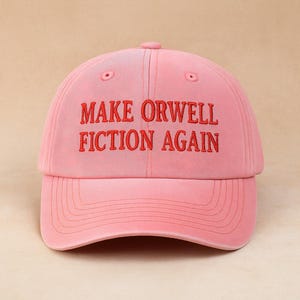 Könnte beinhalten: Eine rosa Baseballkappe mit dem Schriftzug "MAKE ORWELL FICTION AGAIN" in Rot gestickt. Die Kappe hat einen gebogenen Schirm und einen verstellbaren Riemen. Der Hut ist aus weichem Material und einfarbig rosa.