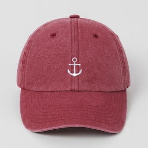 Puede incluir: Gorra de béisbol granate con visera curva. La gorra presenta un ancla blanca bordada en la parte delantera. El sombrero está hecho de una tela suave y texturizada y tiene un diseño clásico de seis paneles.