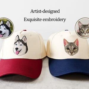 Könnte beinhalten: Zwei Baseballkappen mit künstlerisch gestalteter, exquisiter Stickerei. Eine Kappe hat einen roten Schirm und zeigt ein Husky-Hundeporträt. Die andere hat einen marineblauen Schirm und ein Katzenporträt. Die Kappen sind cremefarben.