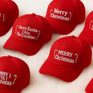 Könnte beinhalten: Rote Baseballkappen mit weiß gesticktem Text. Die Aufschriften lauten "Merry Christmas", "Sorry Santa I Ate The Cookies" und "Team Santa". Einige Texte werden von Zuckerstangen-Grafiken begleitet. Die Kappen sind auf einer weißen Oberfläche angeordnet.