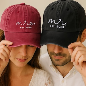 Könnte beinhalten: Zwei Baseballkappen, eine weinrote und eine schwarze. Auf der weinroten Kappe steht "mrs. est. 2025" in weißer Schrift. Auf der schwarzen Kappe steht "mr. est. 2025" in weißer Schrift.