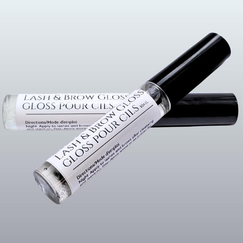 May include: Two clear glass tubes of lash and brow gloss with black caps. The tubes have white labels with the text "LASH & BROW GLOSS GLOSS POUR CILS" and directions. The product is 10ml.