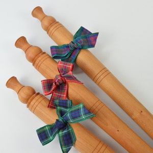 May include: Three wooden rolling pins with decorative handles, each tied with a different plaid ribbon bow in red, green, and blue.