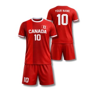 Op de afbeelding: Rode voetbalset bestaande uit een shirt en een korte broek. Het shirt toont "CANADA" en het nummer "10" in het wit, samen met een Canadese vlag. De achterkant van het shirt toont "YOUR NAME" en het nummer "10".