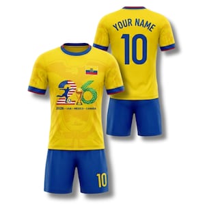 May include: A yellow soccer uniform with blue shorts. The jersey features a design with the number 26, a soccer ball, and the text "2026 - USA - MEXICO - CANADA". The back of the jersey has the number 10 and the words "YOUR NAME".
