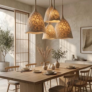 May include: A cluster of five pendant lights with textured, off-white, bell-shaped shades suspended from the ceiling. The shades have an organic, fibrous appearance and emit a warm, soft glow, illuminating the dining area below them.