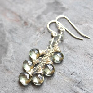May include: Silver dangle earrings with multiple light green faceted gemstone drops. The earrings are made with wire wrapped around the stones and a silver chain.