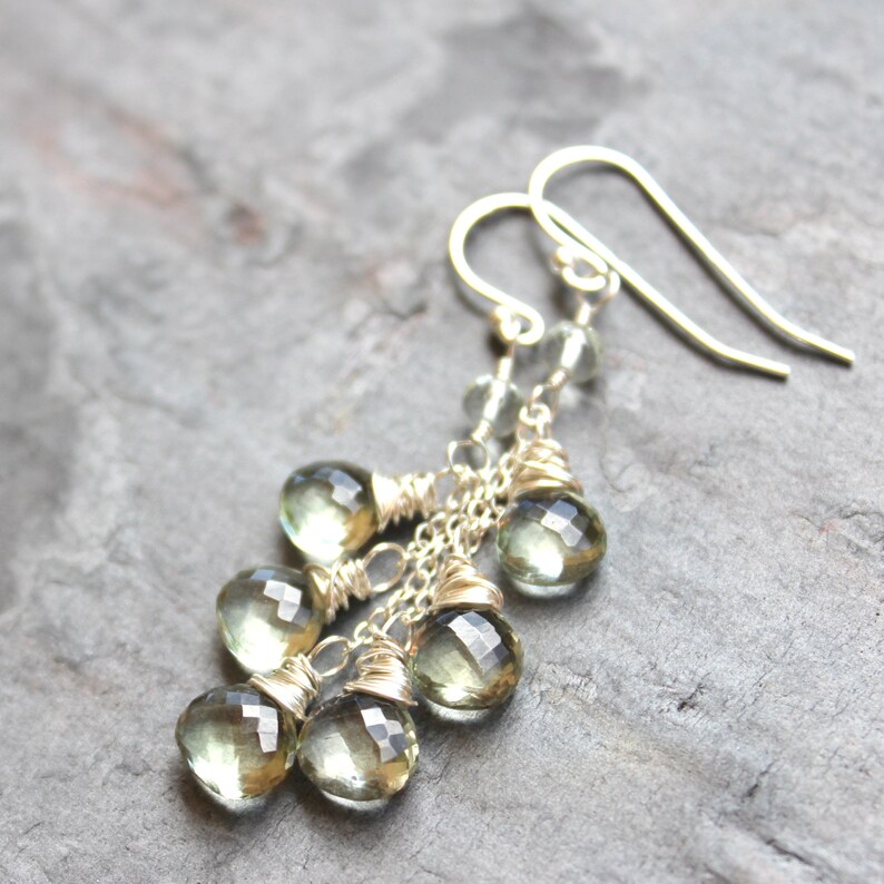 May include: Silver dangle earrings with multiple light green faceted gemstone drops. The earrings are made with wire wrapped around the stones and a silver chain.