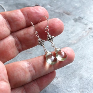 Op de afbeelding: Een paar zilveren oorhangers met groene edelsteen druppels. De oorbellen hebben een zilveren kralencluster aan de bovenkant van de druppel.