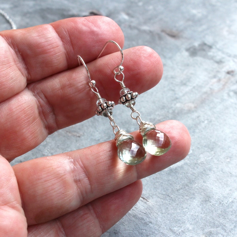 Op de afbeelding: Een paar zilveren oorhangers met groene edelsteen druppels. De oorbellen hebben een zilveren kralencluster aan de bovenkant van de druppel.
