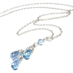 May include: A delicate silver necklace featuring a chain and a pendant with three faceted, light blue teardrop-shaped gemstones. The pendant is wire-wrapped and hangs below a smaller, round gemstone.