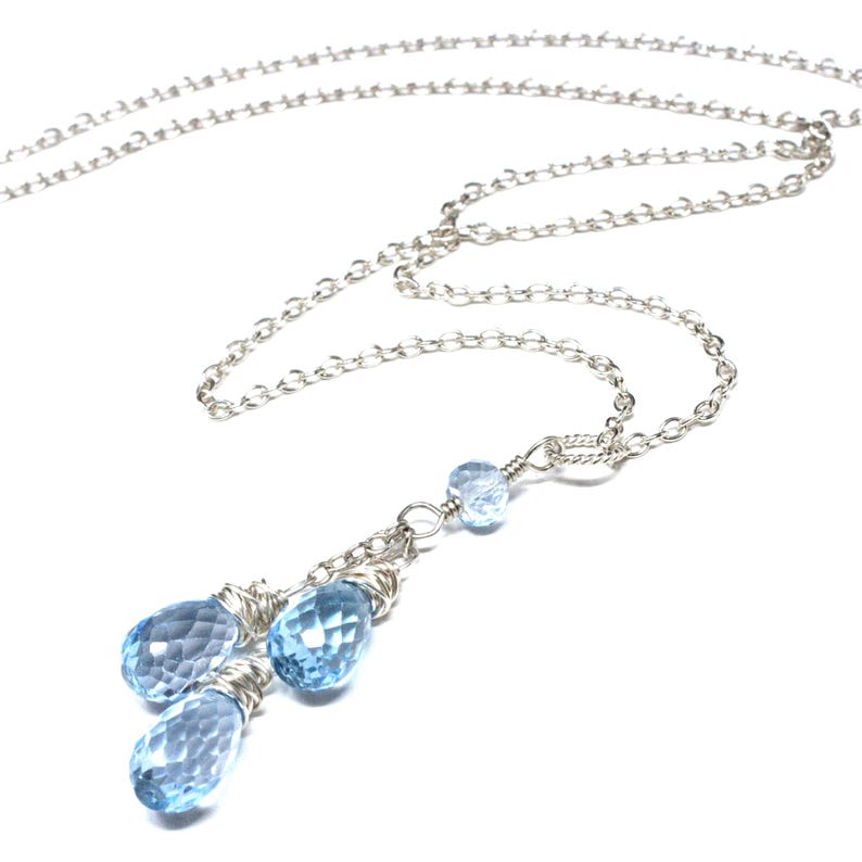 May include: A delicate silver necklace featuring a chain and a pendant with three faceted, light blue teardrop-shaped gemstones. The pendant is wire-wrapped and hangs below a smaller, round gemstone.