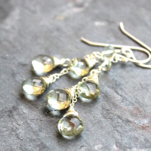 May include: A pair of silver dangle earrings with multiple teardrop-shaped green gemstones. The gemstones are faceted and have a light green color.