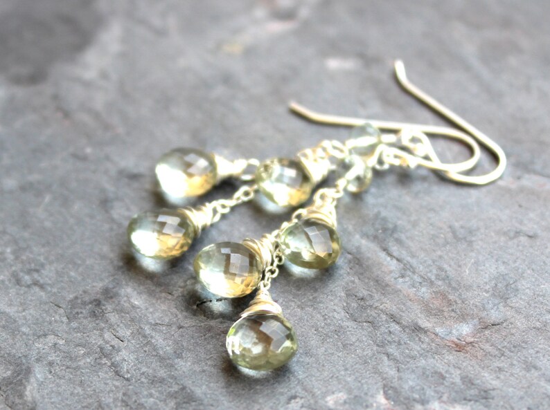 May include: A pair of silver dangle earrings with multiple teardrop-shaped green gemstones. The gemstones are faceted and have a light green color.