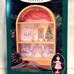 May include: A Hallmark Keepsake Ornament box featuring The Nutcracker Ballet display stage. The box shows a two-tiered wooden stage with a ballerina figurine, a Christmas tree, and candy cane illustrations. A small ballerina ornament is shown.