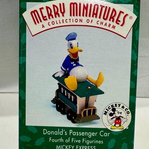 May include: A boxed "Merry Miniatures" collectible featuring Donald Duck seated on a green and white passenger car. The box has a red border with holly leaves and the Mickey & Co. logo.