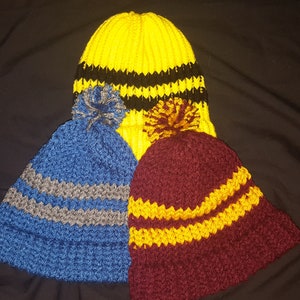 Könnte beinhalten: Drei gestrickte Mützen mit Bommeln. Eine Mütze ist gelb mit schwarzen Streifen, eine ist blau mit grauen Streifen und eine ist dunkelrot mit gelben Streifen.