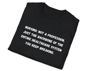 Puede incluir: Camiseta negra con texto blanco: "NURSING: NOT A PROFESSION, JUST THE BACKBONE OF THE ENTIRE HEALTHCARE SYSTEM YOU KEEP BREAKING." La camiseta está doblada y aislada sobre un fondo blanco.