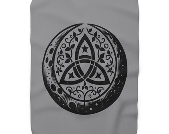 May include: A gray blanket featuring a black, circular design. The design includes a Celtic knot, stars, and floral elements within a moon-like shape. The blanket has a soft, textured appearance.