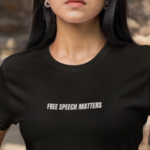 May include: Black t-shirt with the white text "FREE SPEECH MATTERS" across the front. The shirt has a crew neck and short sleeves. The image shows the upper body of a person wearing the t-shirt.