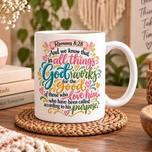 May include: A white ceramic mug featuring the text Romans 8:28 and the quote And we know that in all things God works for the good of those who love him, who have been called according to his purpose, decorated with colourful swirls and hearts.