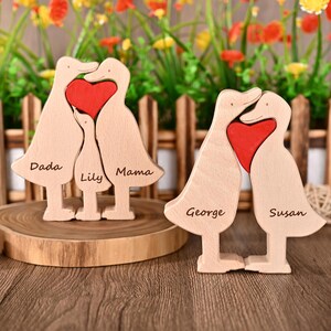 May include: Wooden family duck figurines with a red heart in the centre. One set has the names "Dada", "Lily", and "Mama" engraved. The other set has "George" and "Susan" engraved. The ducks are light brown.