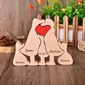 May include: A wooden family sculpture of five duck-shaped figures. The central ducks form a heart shape with a red heart insert. Names are engraved on each duck: Karen, Sam, Susan, Jeulia, and Claire. The sculpture is made of light-coloured wood.