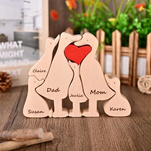 May include: Wooden family ornament depicting duck-shaped figures with a red heart. The names "Claire", "Dad", "Jeulia", "Mom", "Susan", and "Karen" are engraved. A decorative item for home decor, ideal for a family.