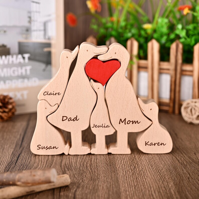May include: Wooden family ornament depicting duck-shaped figures with a red heart. The names "Claire", "Dad", "Jeulia", "Mom", "Susan", and "Karen" are engraved. A decorative item for home decor, ideal for a family.