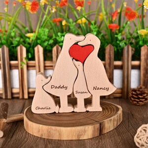 May include: Wooden family sculpture with duck-shaped figures and a red heart. The names "Daddy", "Susan", "Nancy", and "Charlie" are engraved on the figures. The sculpture is displayed on a wooden slice.