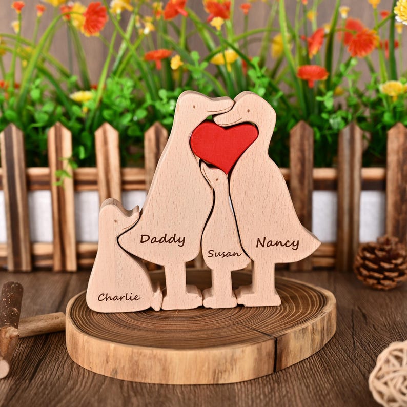 May include: Wooden family sculpture with duck-shaped figures and a red heart. The names "Daddy", "Susan", "Nancy", and "Charlie" are engraved on the figures. The sculpture is displayed on a wooden slice.