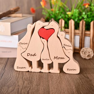 May include: Wooden family duck puzzle with a red heart in the centre. The names "Claire", "Dad", "Susan", "Jeulia", "Mom", "Kevin", and "Karen" are engraved on the ducks. A decorative item for the home.