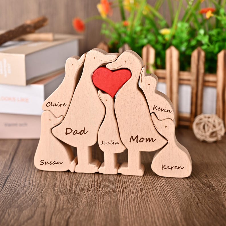 May include: Wooden family duck puzzle with a red heart in the centre. The names "Claire", "Dad", "Susan", "Jeulia", "Mom", "Kevin", and "Karen" are engraved on the ducks. A decorative item for the home.